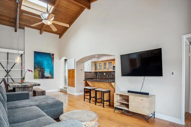 living room featuring ceiling fan, beam ceiling, light wood finished floors, arched walkways, and wood ceiling