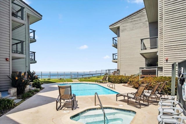 pool featuring a water view, a hot tub, and a patio area