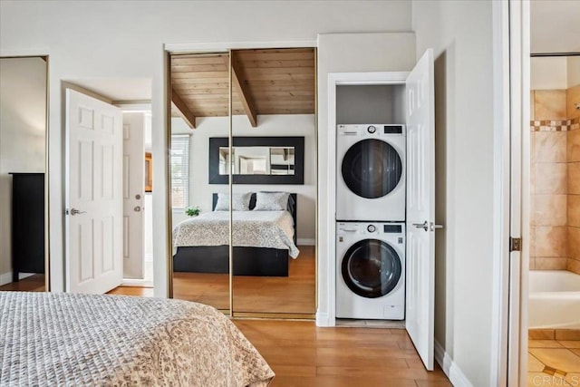 bedroom with baseboards, wood ceiling, stacked washing maching and dryer, and wood finished floors