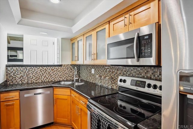 kitchen with a sink, dark stone counters, decorative backsplash, and stainless steel appliances