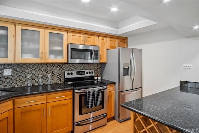 kitchen with appliances with stainless steel finishes, tasteful backsplash, light wood-type flooring, and dark stone countertops