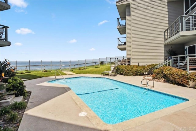 pool with a patio, a water view, and fence