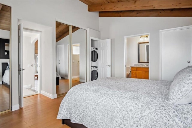 bedroom featuring baseboards, vaulted ceiling with beams, wood finished floors, stacked washer and clothes dryer, and a closet