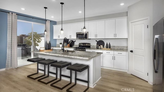 32798 Crystal Cove Ct, Winchester, CA 92596 - kitchen with white cabinets, a sink, stainless steel appliances, light wood-type flooring, and a center island with sink