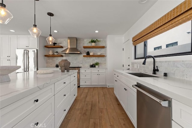 kitchen with wall chimney range hood, backsplash, appliances with stainless steel finishes, open shelves, and a sink