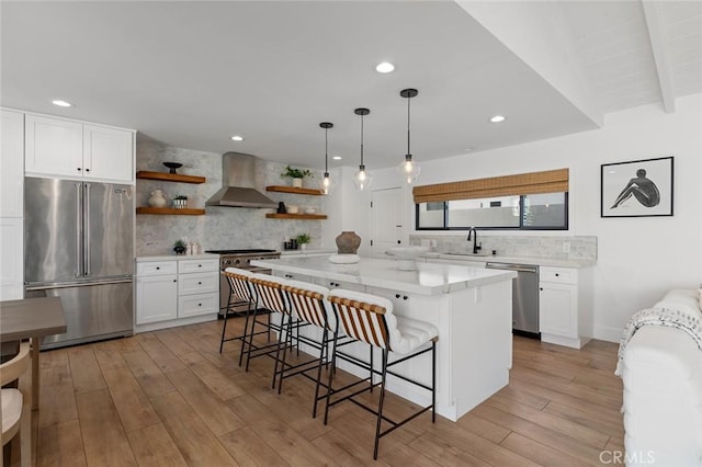 kitchen with open shelves, decorative backsplash, wall chimney range hood, a sink, and premium appliances