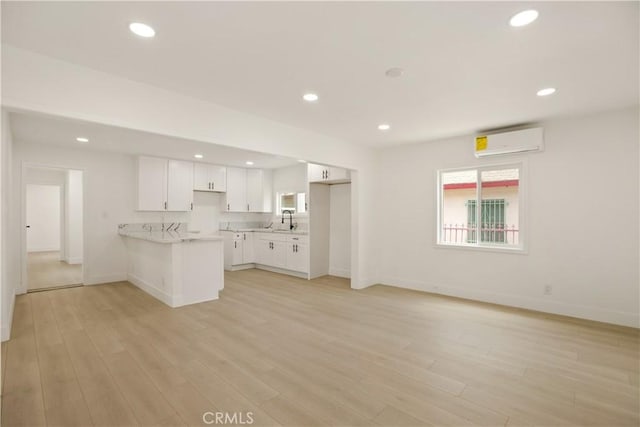 kitchen with a peninsula, an AC wall unit, light countertops, white cabinets, and a sink