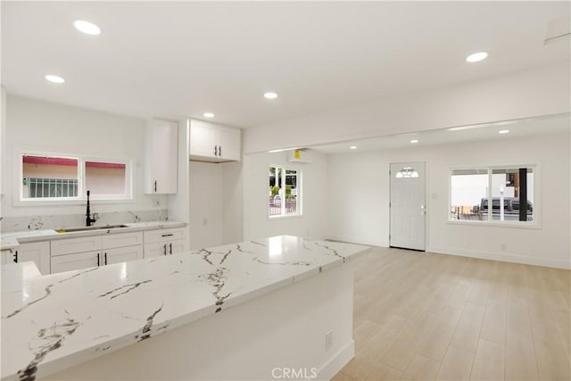 kitchen with light stone counters, a sink, light wood-style flooring, white cabinetry, and recessed lighting