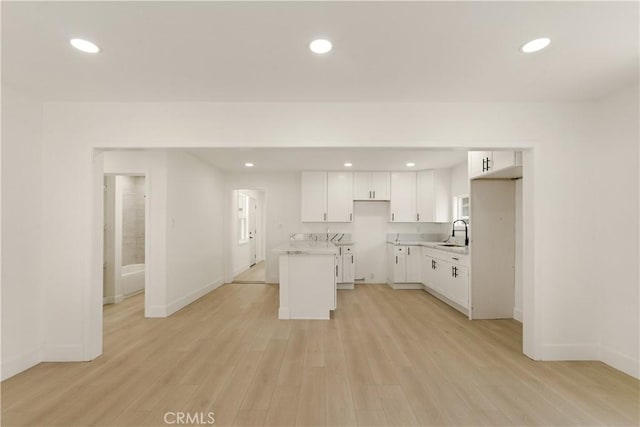 kitchen with baseboards, recessed lighting, light countertops, a sink, and light wood-style flooring