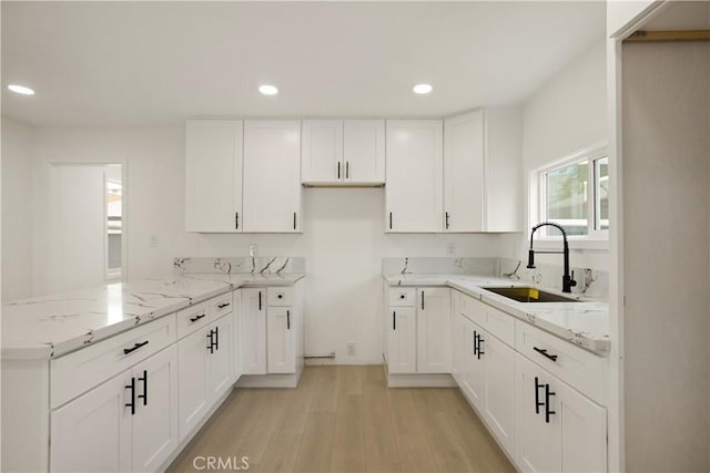 kitchen with a peninsula, white cabinetry, light stone counters, a sink, and light wood finished floors