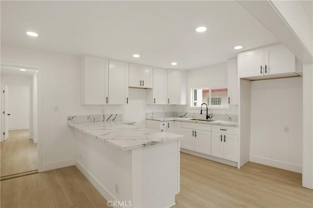 kitchen with white cabinetry, a sink, and light wood-style flooring