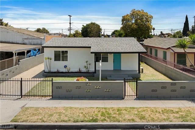 view of front of house featuring a fenced front yard, a front yard, a gate, a shingled roof, and stucco siding