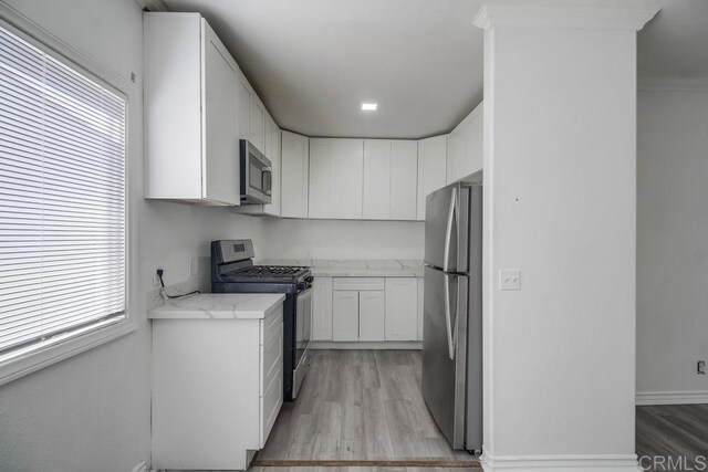 kitchen with white cabinets, stainless steel appliances, light stone counters, and light wood-type flooring
