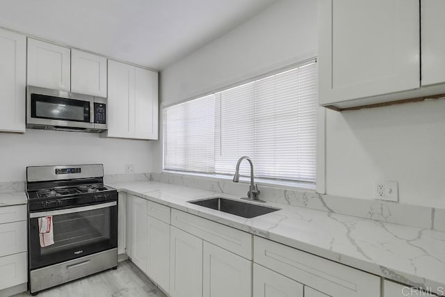 kitchen featuring a sink, appliances with stainless steel finishes, white cabinets, and light stone countertops