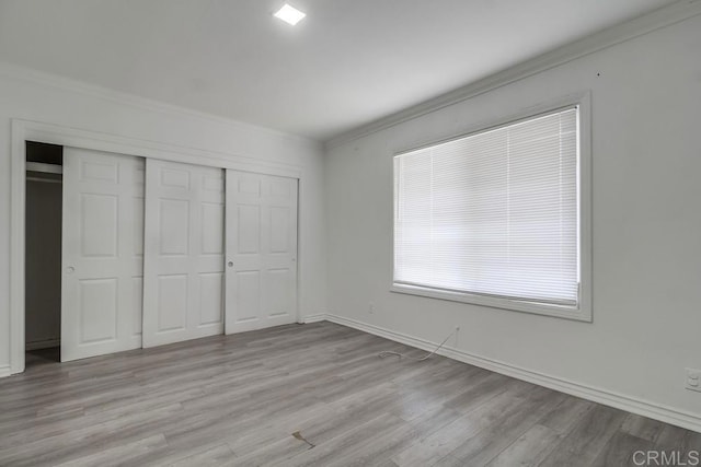 unfurnished bedroom featuring a closet, ornamental molding, light wood-style flooring, and baseboards
