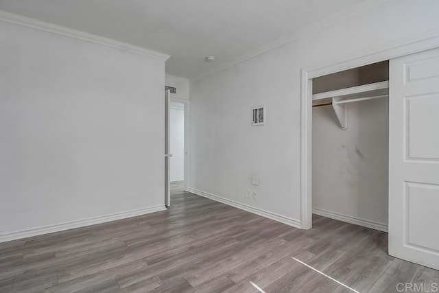 unfurnished bedroom featuring baseboards, ornamental molding, wood finished floors, and a closet