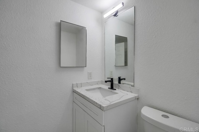 half bathroom featuring vanity, a textured wall, and toilet
