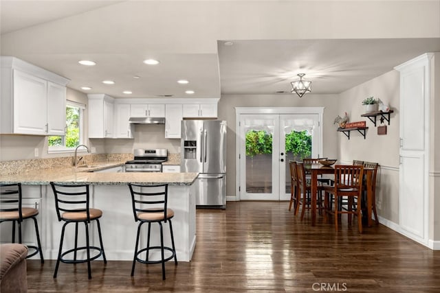 kitchen featuring appliances with stainless steel finishes, a sink, white cabinets, a peninsula, and under cabinet range hood