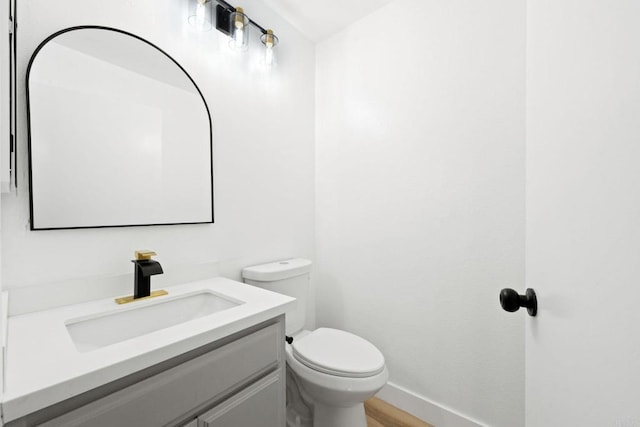 half bath featuring vanity, baseboards, and toilet