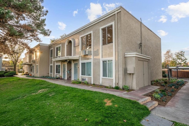 rear view of property with a lawn, fence, and stucco siding
