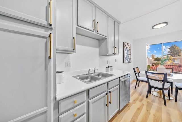 kitchen featuring stainless steel dishwasher, light wood-type flooring, light countertops, gray cabinets, and a sink