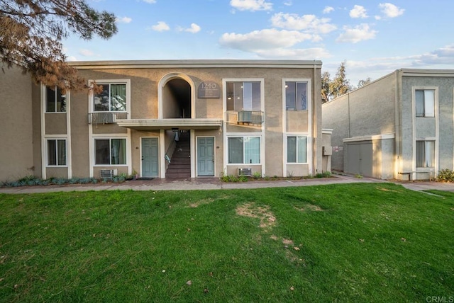 view of front of house featuring a balcony, stairs, stucco siding, and a front yard