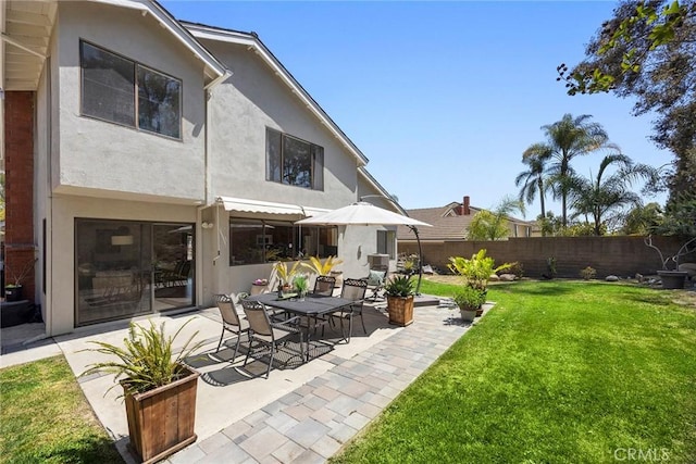 rear view of house with a fenced backyard, stucco siding, a yard, and a patio area