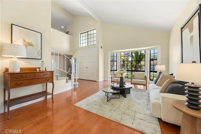 living area with stairway, high vaulted ceiling, baseboards, and wood finished floors