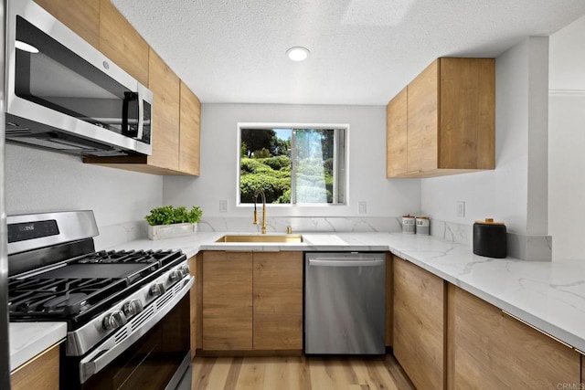 kitchen with brown cabinets, appliances with stainless steel finishes, light stone counters, a sink, and light wood finished floors