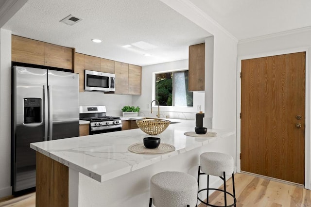 kitchen with visible vents, light stone countertops, light wood finished floors, a peninsula, and stainless steel appliances