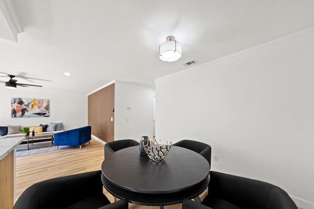 dining area with ceiling fan, light wood-style flooring, baseboards, visible vents, and ornamental molding