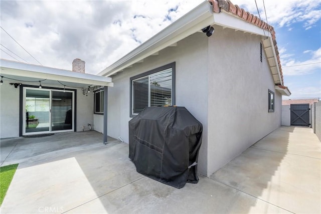 exterior space with a gate, a patio area, stucco siding, and a chimney