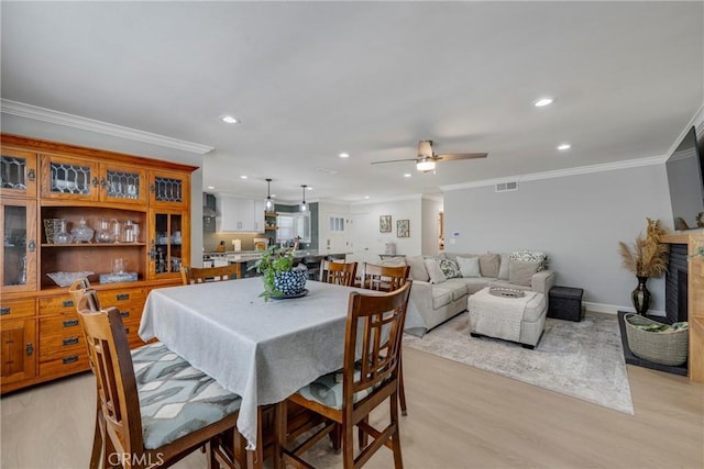 dining area with ceiling fan, a fireplace with raised hearth, recessed lighting, light wood-type flooring, and ornamental molding