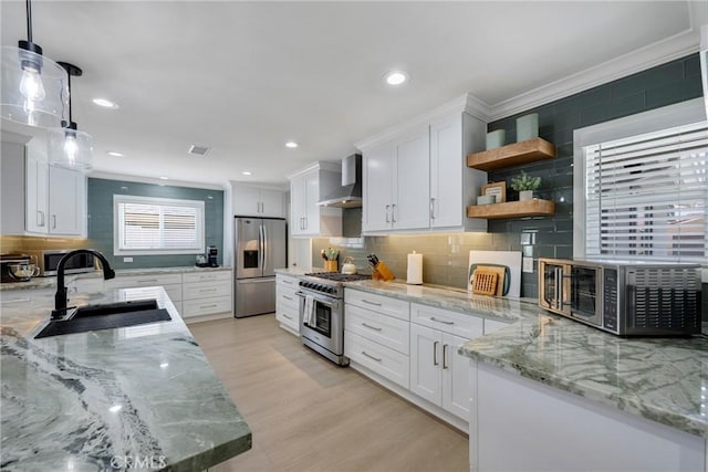 kitchen featuring wall chimney range hood, appliances with stainless steel finishes, a sink, tasteful backsplash, and ornamental molding