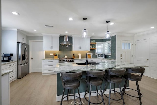 kitchen featuring visible vents, ornamental molding, wall chimney range hood, stainless steel fridge, and a sink