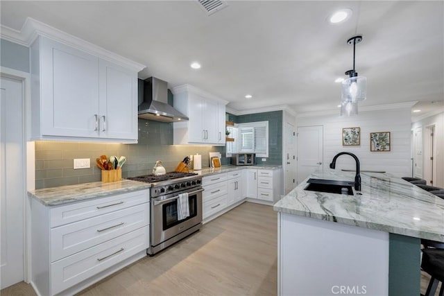 kitchen with stainless steel stove, a sink, crown molding, and wall chimney range hood
