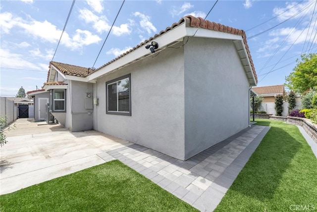view of home's exterior with fence, a tile roof, stucco siding, a gate, and a yard