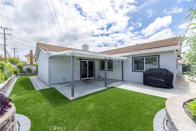 back of property featuring stucco siding, a chimney, a patio, a tiled roof, and a yard