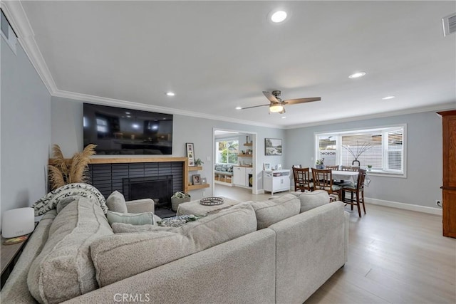 living area with crown molding, recessed lighting, light wood-style flooring, and a brick fireplace