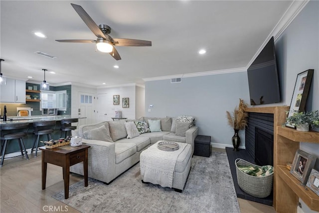 living room with visible vents, ornamental molding, ceiling fan, light wood-type flooring, and a fireplace with raised hearth