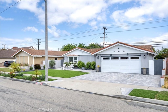ranch-style home featuring decorative driveway, a garage, a front lawn, and a tile roof