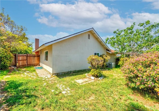 view of property exterior featuring a chimney, central AC, fence, a yard, and stucco siding