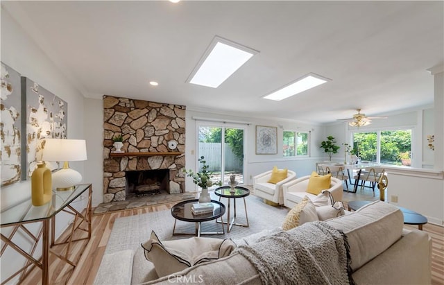 living room featuring a stone fireplace, crown molding, wood finished floors, and a wealth of natural light