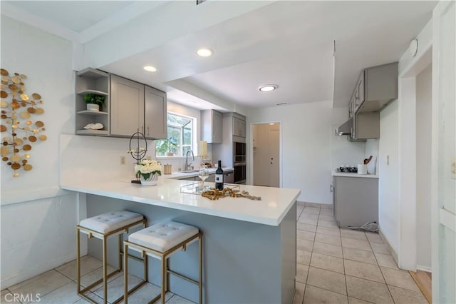 kitchen featuring light countertops, a breakfast bar area, gray cabinets, a peninsula, and light tile patterned floors