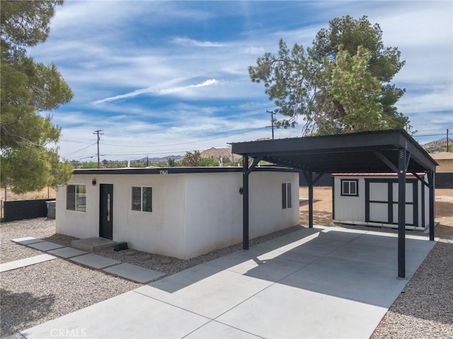 rear view of property with a storage shed, an outbuilding, a detached carport, concrete driveway, and stucco siding