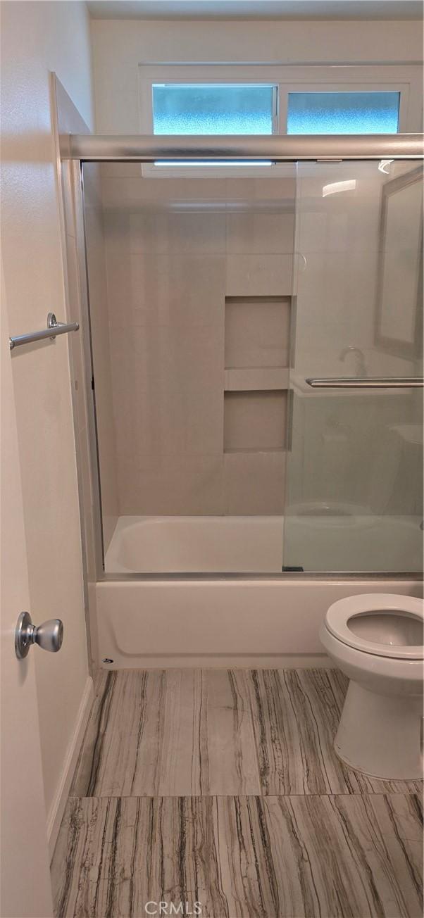 bathroom with toilet and shower / bath combination with glass door
