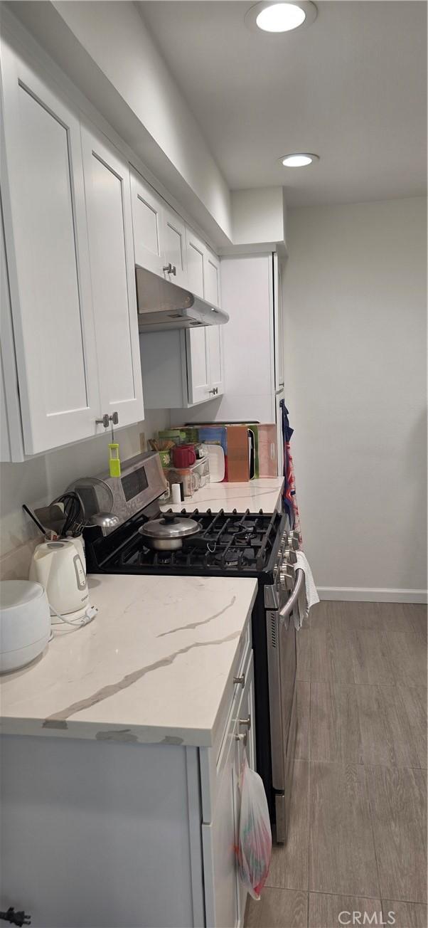 kitchen with light wood-style flooring, under cabinet range hood, stainless steel gas stove, and white cabinetry