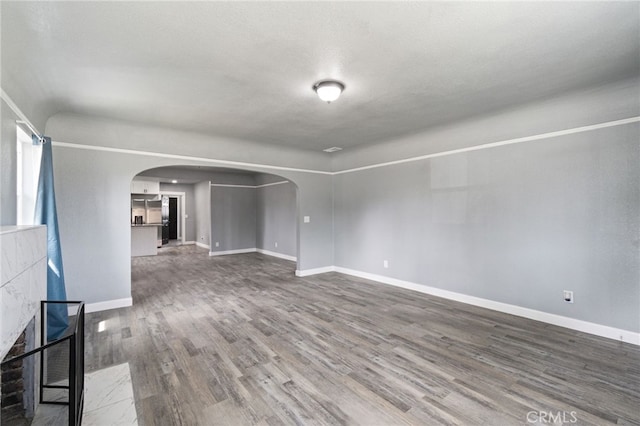 unfurnished living room featuring arched walkways, baseboards, and wood finished floors