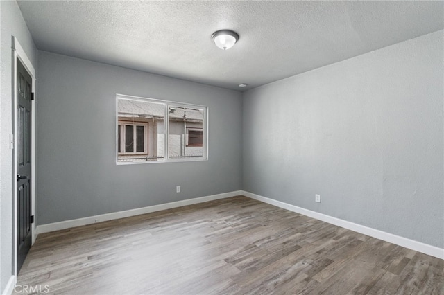 spare room featuring a textured ceiling, baseboards, and wood finished floors