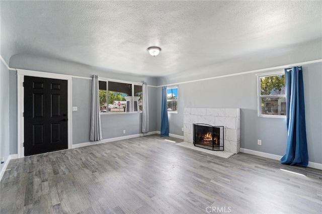 unfurnished living room featuring a healthy amount of sunlight, a textured ceiling, a fireplace, and wood finished floors